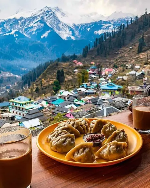 A plate of momos and glasses of tea on a table, a mountain village behind